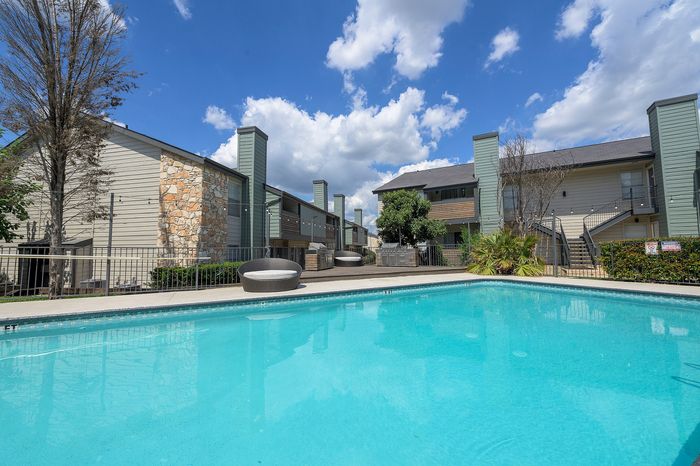 Inviting apartment complex with a refreshing outdoor pool, surrounded by modern buildings under a clear blue sky.