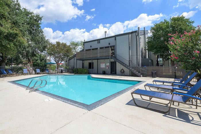Inviting outdoor pool area with modern loungers and lush greenery, perfect for relaxing under sunny skies.