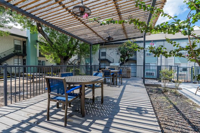 Inviting outdoor patio with modern seating under a stylish pergola, surrounded by lush greenery in a charming apartment complex.