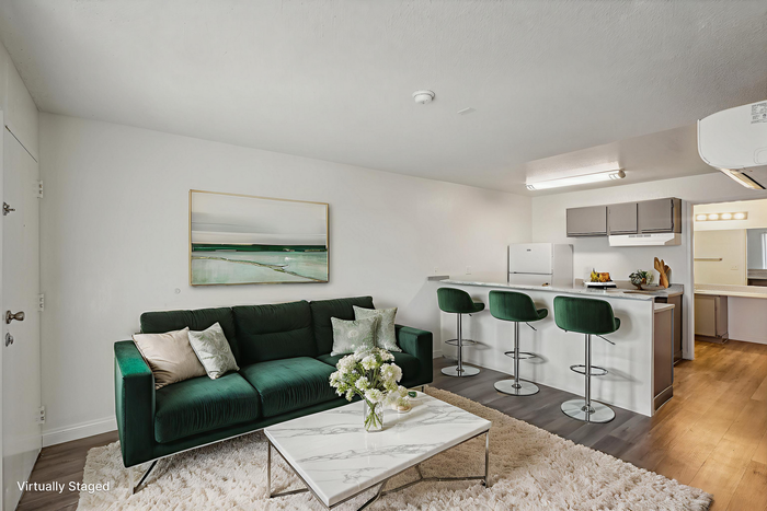 Chic and modern living room with plush green sofa, elegant marble coffee table, and sleek kitchen with bar stools, seamlessly merging style and comfort.