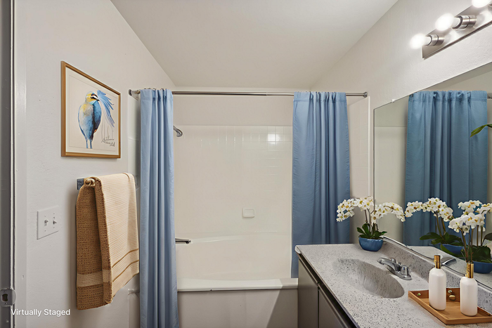 Chic bathroom with elegant blue curtains, a charming bird painting, and fresh floral accents for a serene atmosphere.