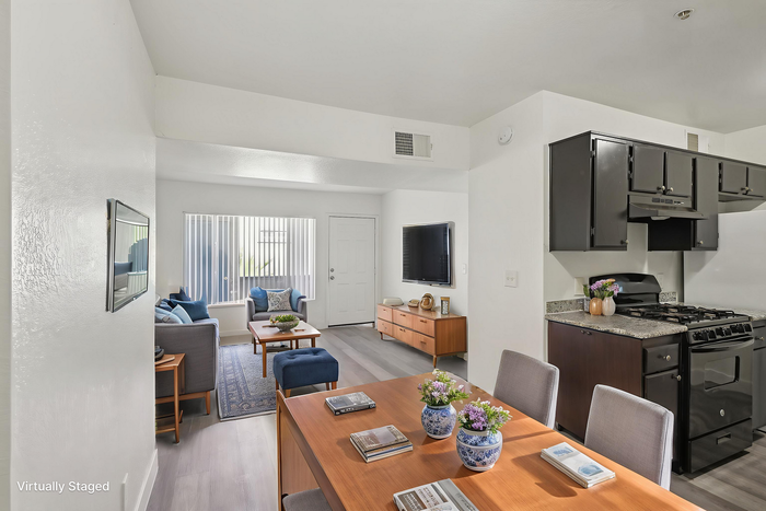 Bright, virtually staged open-plan living and kitchen area with modern d&eacute;cor, featuring sleek black cabinetry and elegant furnishings.