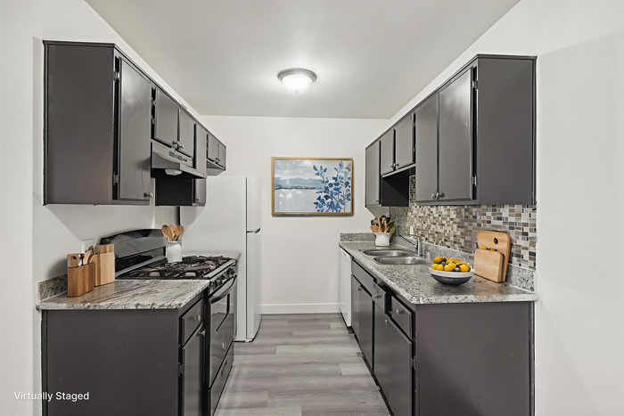 Modern kitchen with sleek dark cabinets, granite countertops, and stylish backsplash, featuring stainless steel appliances and elegant staging.
