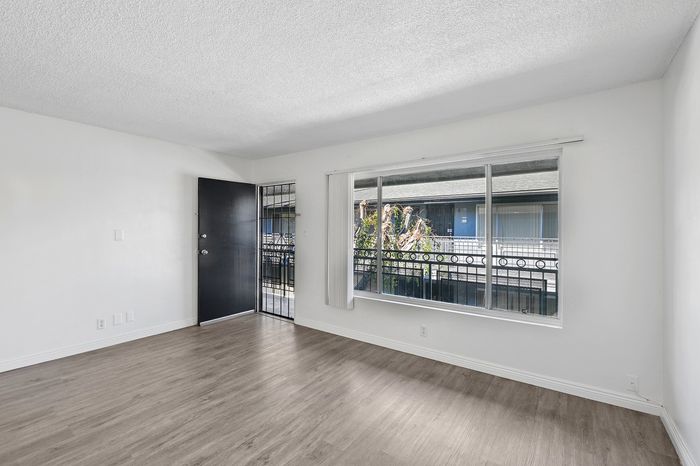 Bright and inviting apartment interior with large window, sleek wood flooring, and open entrance, perfect for modern living.