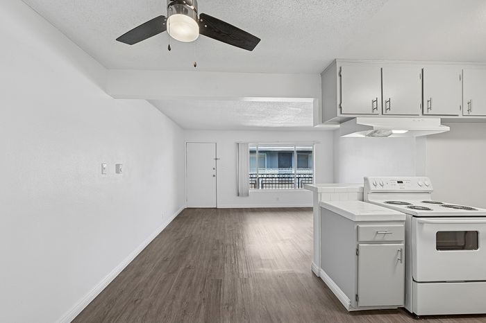 Welcoming open-concept apartment with sleek wood flooring, modern kitchen, and ample natural light from a large window.