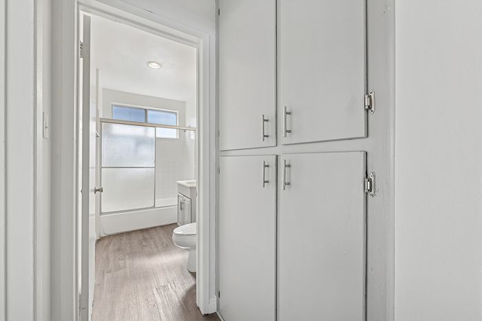 Bright modern bathroom with crisp white cabinetry, enclosed shower, and wood-style flooring, offering a sleek and refreshing ambiance.
