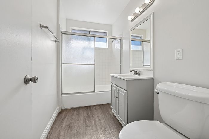 Bright modern bathroom with crisp white cabinetry, enclosed shower, and wood-style flooring, offering a sleek and refreshing ambiance.