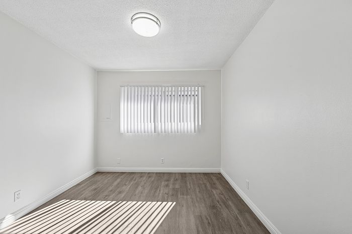 Bright, minimalist room with elegant wooden flooring and a large window featuring vertical blinds, perfect for a cozy setup.
