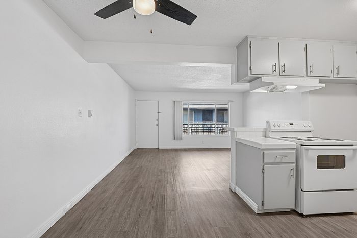 Bright and open living space with modern laminate flooring, sleek ceiling fan, and an inviting kitchen area ideal for cozy gatherings.