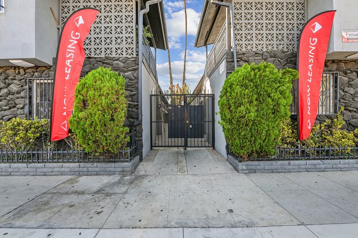 Inviting apartment entrance with lush greenery and vibrant 'Now Leasing' banners.