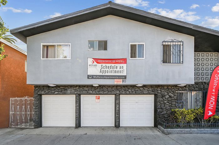Charming apartment building with stone accents and large garage doors, featuring a prominent banner inviting visitors to schedule appointments at Westland @ Daisy for premier living solutions.