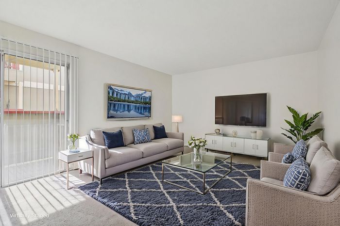 Bright, modern living room with chic furniture, large TV, and elegant decor, featuring a sunlit window and plush blue rug.