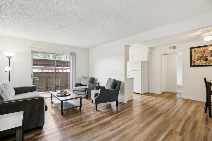 Bright and inviting living room with cozy seating, elegant hardwood floors, and access to a sunlit balcony in a modern apartment.