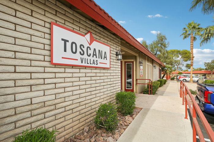 Inviting exterior view of Toscana Villas, showcasing a charming entrance, lush greenery, and a sunny blue sky.