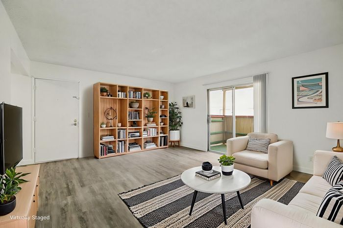 Chic living room with a minimalistic design, featuring sleek hardwood floors, a modern entertainment center, an elegant bookshelf, and natural light from the patio doors.