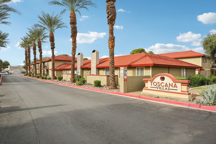 Charming Toscana Villas apartment complex with palm-lined driveway and attractive red tile roofing, offering serene living in a beautiful setting.