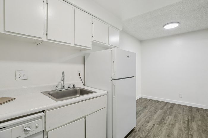 Bright, modern kitchen with sleek white cabinetry, stainless steel sink, and a spacious refrigerator.