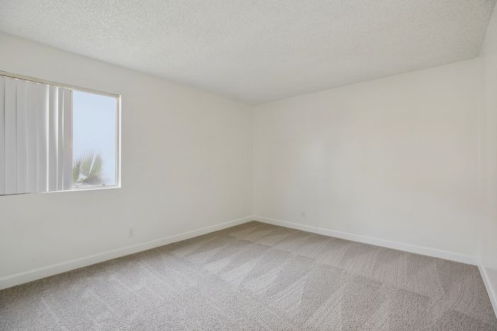 Bright and spacious room with soft carpeting and a large window, featuring modern, minimalist design. Ideal for creating a cozy bedroom or a serene home office.