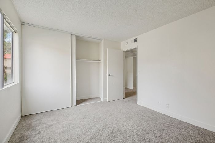 Bright and airy bedroom featuring large window, spacious closet, and soft carpeting, perfect for modern living.