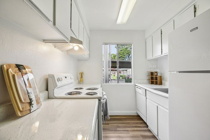 Bright, modern kitchen with sleek white cabinetry, polished countertops, and a scenic window view.