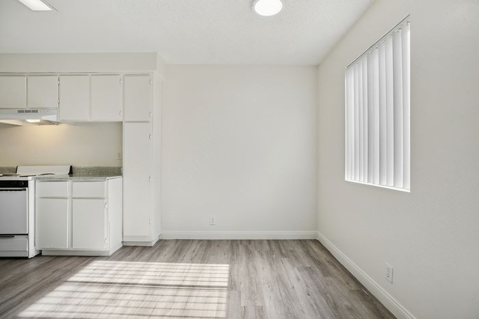 Bright modern kitchen area with sleek white cabinets, elegant countertops, and beautiful natural light through vertical blinds.