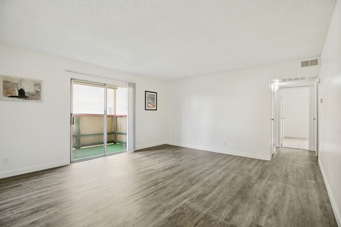 Bright and spacious living area with elegant wood flooring, large sliding doors, and a private balcony, ideal for modern living.