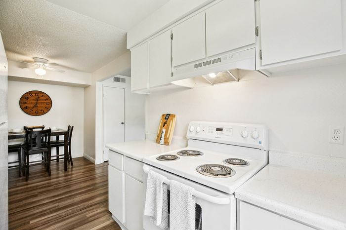 Bright, modern kitchen with sleek white cabinetry, electric stove, and cozy dining area featuring a stylish wooden wall clock.