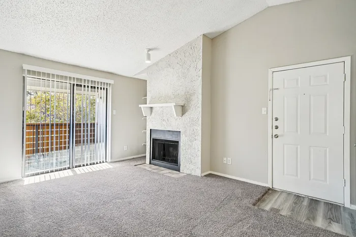 Bright and airy living room with plush carpet, cozy fireplace, and sliding glass doors leading to a private balcony.