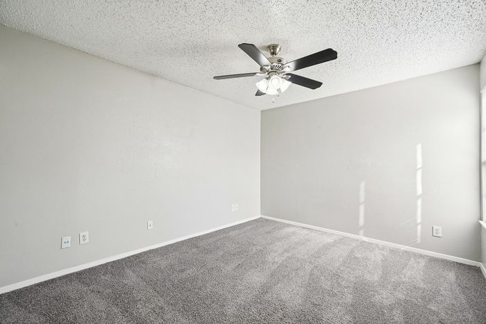 Bright and inviting bedroom with plush carpet, modern ceiling fan, and ample natural light streaming through large windows.