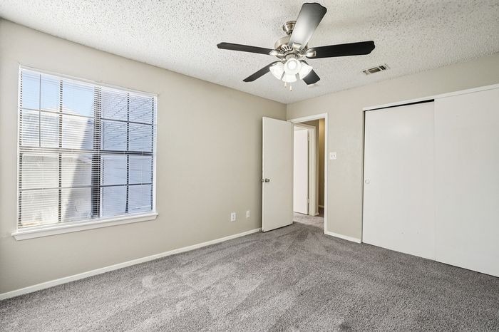 Bright and inviting bedroom with plush carpet, a large window, and a ceiling fan offering comfort and elegance.