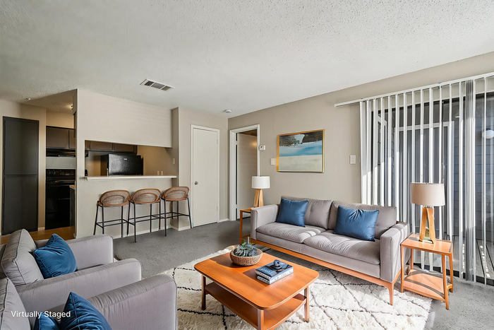 Modern open-concept living room with sleek furnishings, plush gray couches, and a cozy breakfast bar with elegant stools.