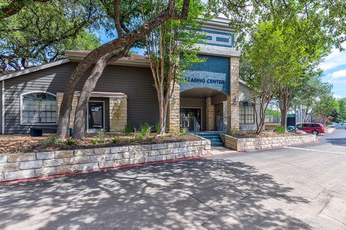 Charming leasing center with stone accents and lush trees creating a welcoming entrance.