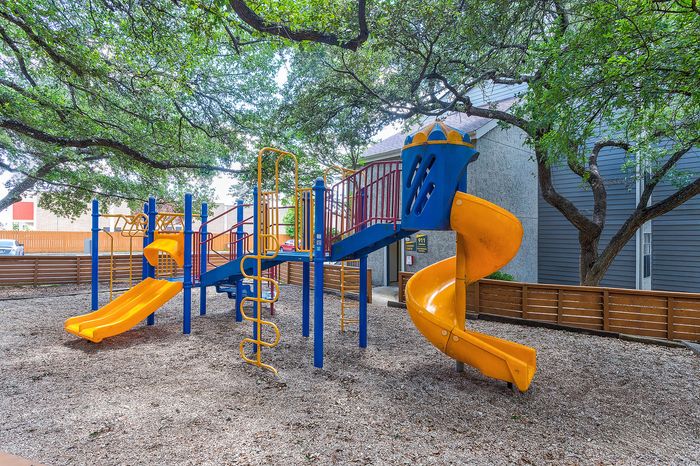 Charming playground with vibrant slides and climbing structures nestled under lush trees, perfect for family fun and outdoor enjoyment.