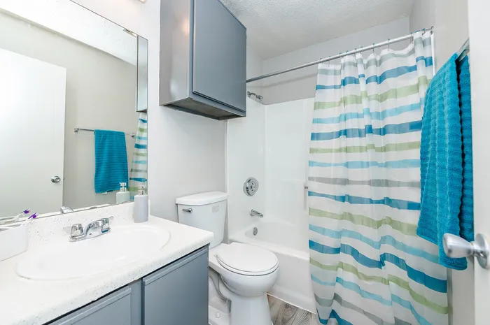 Bright and modern bathroom featuring a sleek white countertop, stylish silver fixtures, and a vibrant striped shower curtain for a fresh, inviting atmosphere.