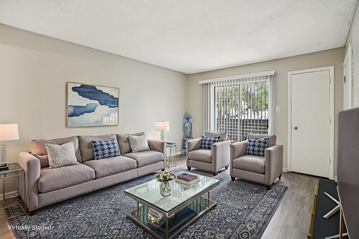 Modern living room with elegant decor, featuring a cozy gray sofa, stylish armchairs, and a chic glass coffee table on a patterned rug.