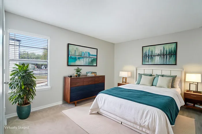 Elegant bedroom featuring a plush bed with teal accents, modern wooden furniture, and large window allowing abundant natural light.