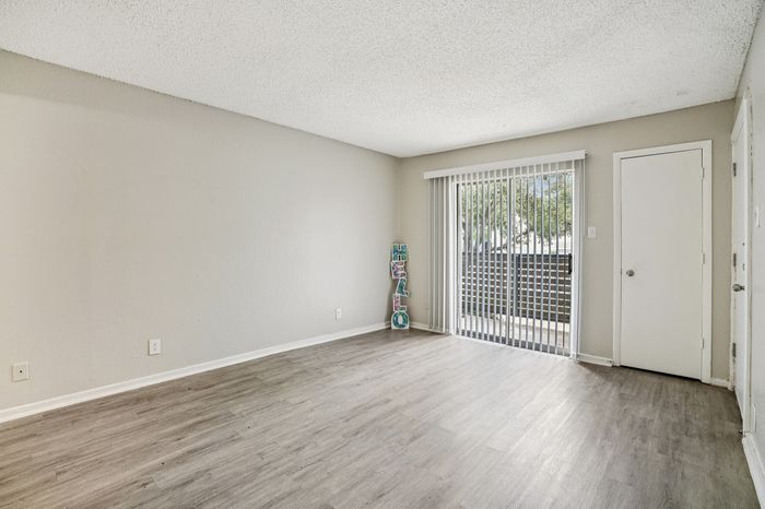 Bright and airy room with sleek wood flooring, large sliding glass doors opening to a patio, and welcoming neutral tones.