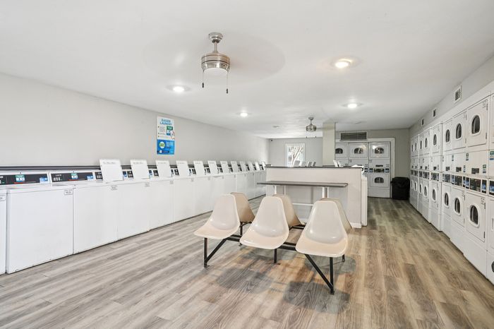 Spacious apartment laundry room featuring modern washers and dryers, sleek flooring, and comfortable seating area.
