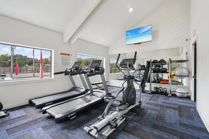 Bright and modern fitness center with treadmills, elliptical, and a variety of exercise equipment set against a sleek mirror wall.