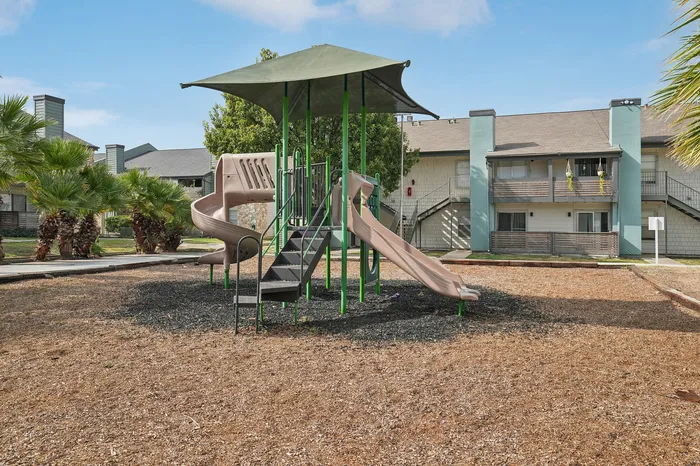 Charming apartment complex with child-friendly playground, vibrant slides, and green surroundings, perfect for family living.