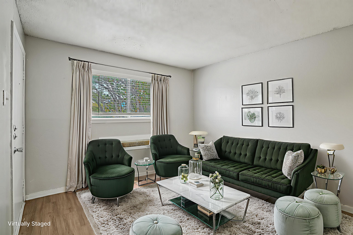 Sleek and cozy living room with plush dark green seating, elegant marble-top coffee table, and tasteful wall art, set against a backdrop of soft beige walls and abundant natural light.