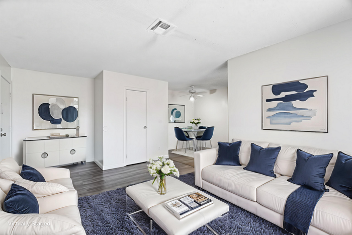 Modern living room with stylish decor, elegant white seating, navy accents, and a cozy dining area, perfect for relaxation and entertainment.