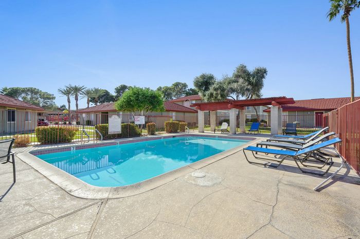 Inviting outdoor pool area with luxurious lounge chairs, vibrant red-roofed buildings, and lush greenery perfect for relaxation and enjoyment.