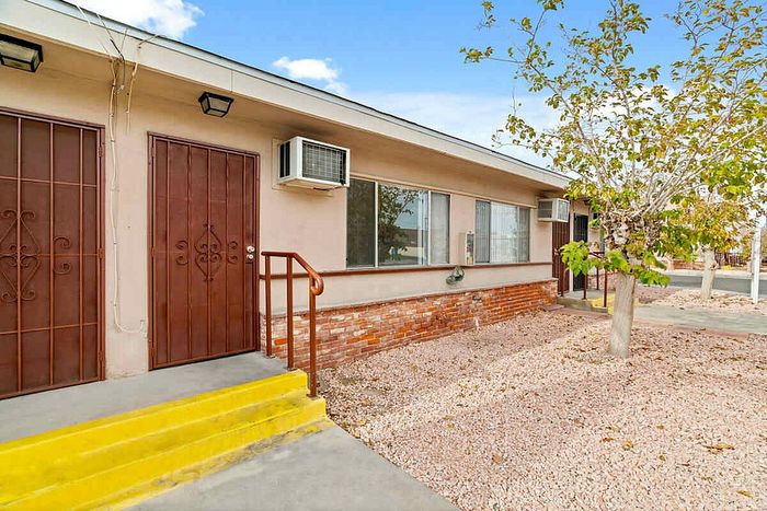 Charming apartment exterior with a welcoming entrance, brick accents, bright yellow steps, and a serene tree-lined yard.