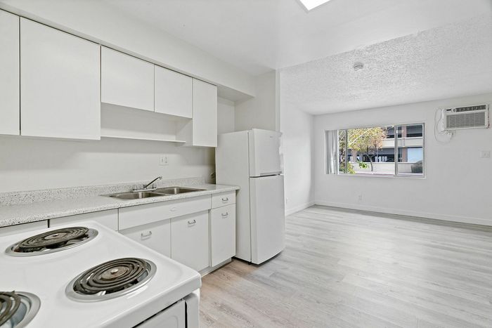 Bright, modern kitchen with sleek white cabinetry, ample countertop space, and sunlit living area featuring large windows and stylish flooring, perfect for welcoming homes.