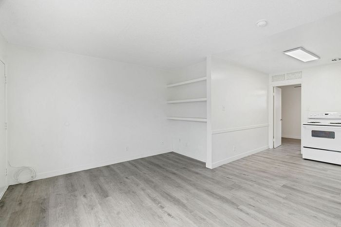 Bright and modern living space with sleek gray flooring, built-in shelves, and a cozy kitchen area.