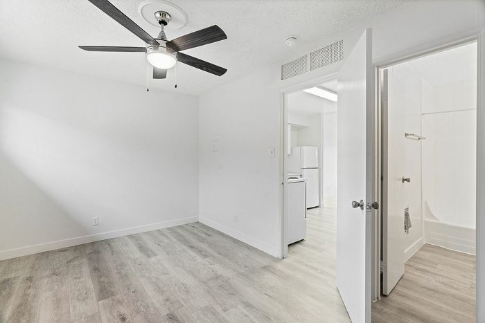 Bright and modern room with sleek gray flooring, stylish ceiling fan, leading to a pristine kitchen and bathroom.