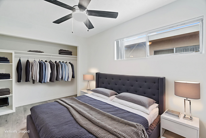 Modern bedroom with plush gray bedding, sleek ceiling fan, and built-in closet showcasing organized clothing space, exuding stylish elegance.
