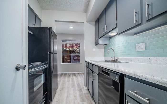Contemporary kitchen with sleek black appliances, ample cabinetry, and stylish mint subway tile backsplash.