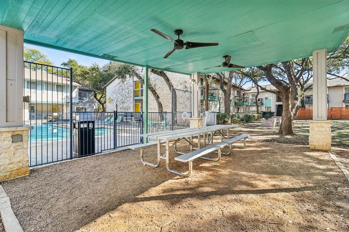 Inviting outdoor picnic area with covered seating and ceiling fans, overlooking a sparkling pool in a charming apartment community.